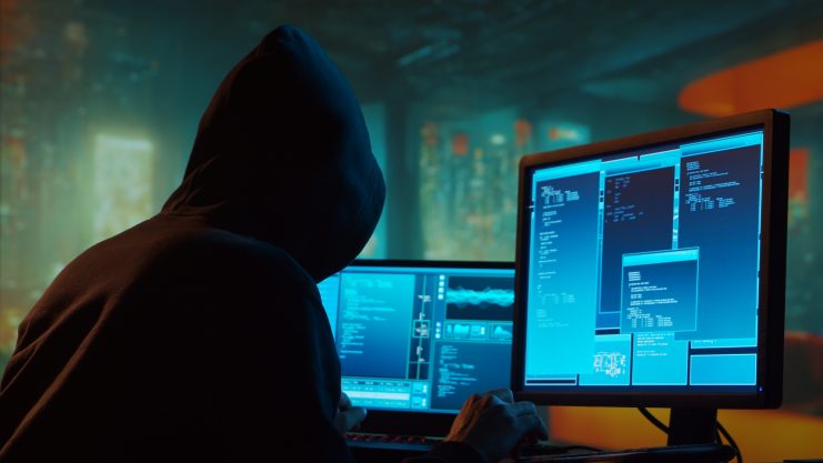 Das Bild zeigt einen Hacker vor einem Bildschirm