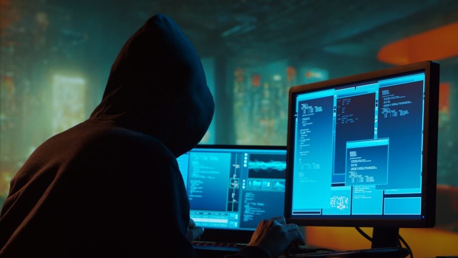 Das Bild zeigt einen Hacker vor einem Bildschirm