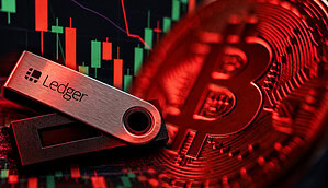 Eine Ledger-Hardware-Wallet vor einer rot beleuchteten Bitcoin-Münze und einem Krypto-Kurschart mit roten und grünen Kerzen. Das Bild symbolisiert Sicherheitsrisiken und mögliche Angriffe auf Ledger-Nutzer.