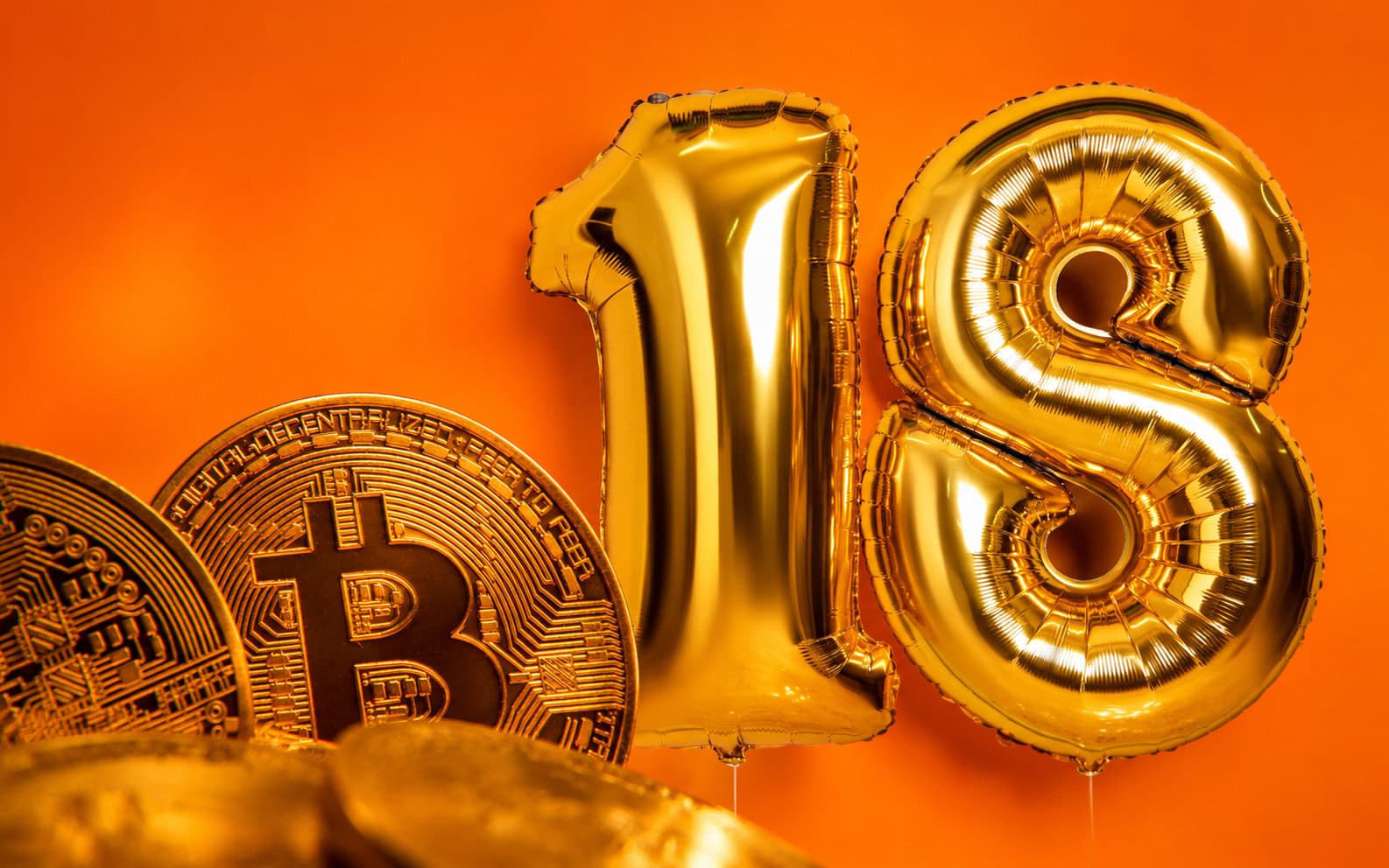 Goldene Luftballons in Form der Zahl 18 neben mehreren Bitcoin-Münzen vor einem orangefarbenen Hintergrund.