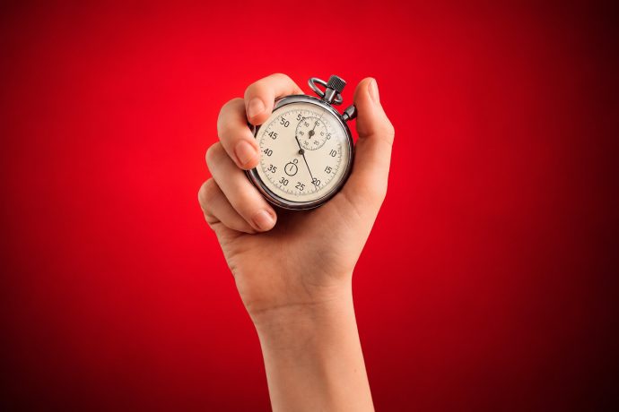 Eine Hand hält eine silberne Stoppuhr vor einem leuchtend roten Krypto-Hintergrund.