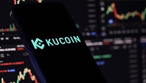Smartphone mit Kucoin Emblem vor dunklem Hintergrund mit Graphen