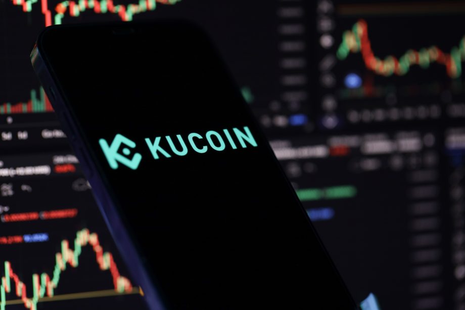 Smartphone mit Kucoin Emblem vor dunklem Hintergrund mit Graphen