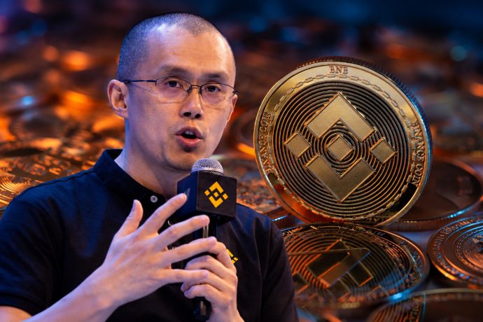 Binance-Gründer Changpeng Zhao (CZ) mit Mikrofon neben einer großen goldenen BNB-Münze.