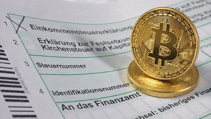 Man sieht ein deutsches Steuerformular und zwei Bitcoin-Münzen.