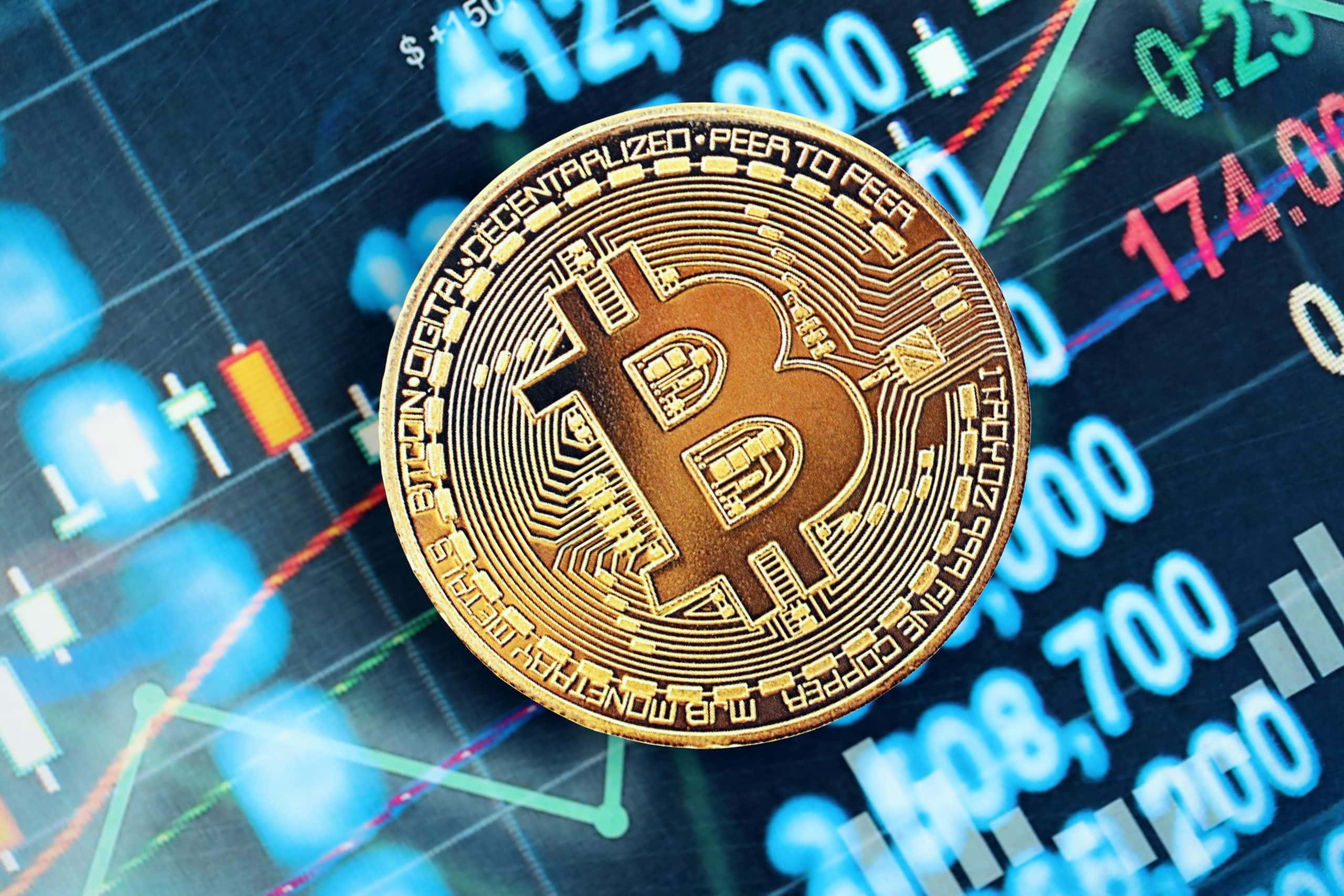 In der Mitte des Bildes sieht man eine Bitcoin-Münze. Im Hintergrund sieht man eine Trading-Oberfläche.