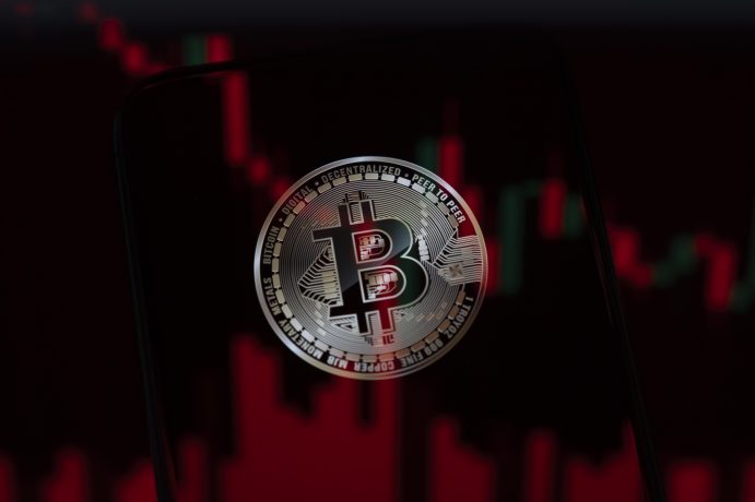 Bitcoin-Münze vor einem roten Kurschart mit fallenden Kerzen
