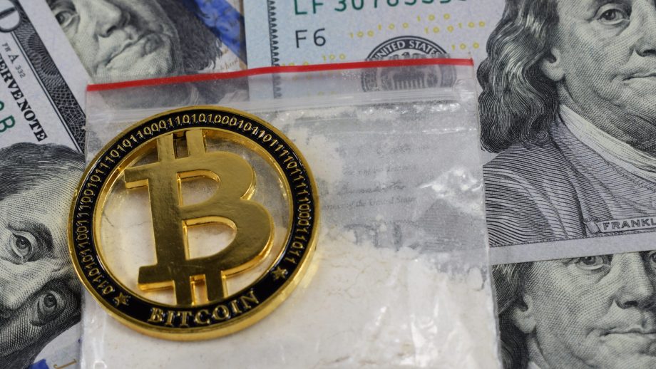 Das Bild zeigt das Bitcoin-Logo auf Drogen und US-Dollar-Scheinen