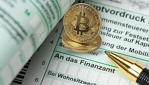 Man sieht einen Vordruck vom Finanzamt. Rechts davon liegt ein Kugelschreiber ab und mittig oben sind zwei Bitcoin-Münzen auf dem Formular positioniert.