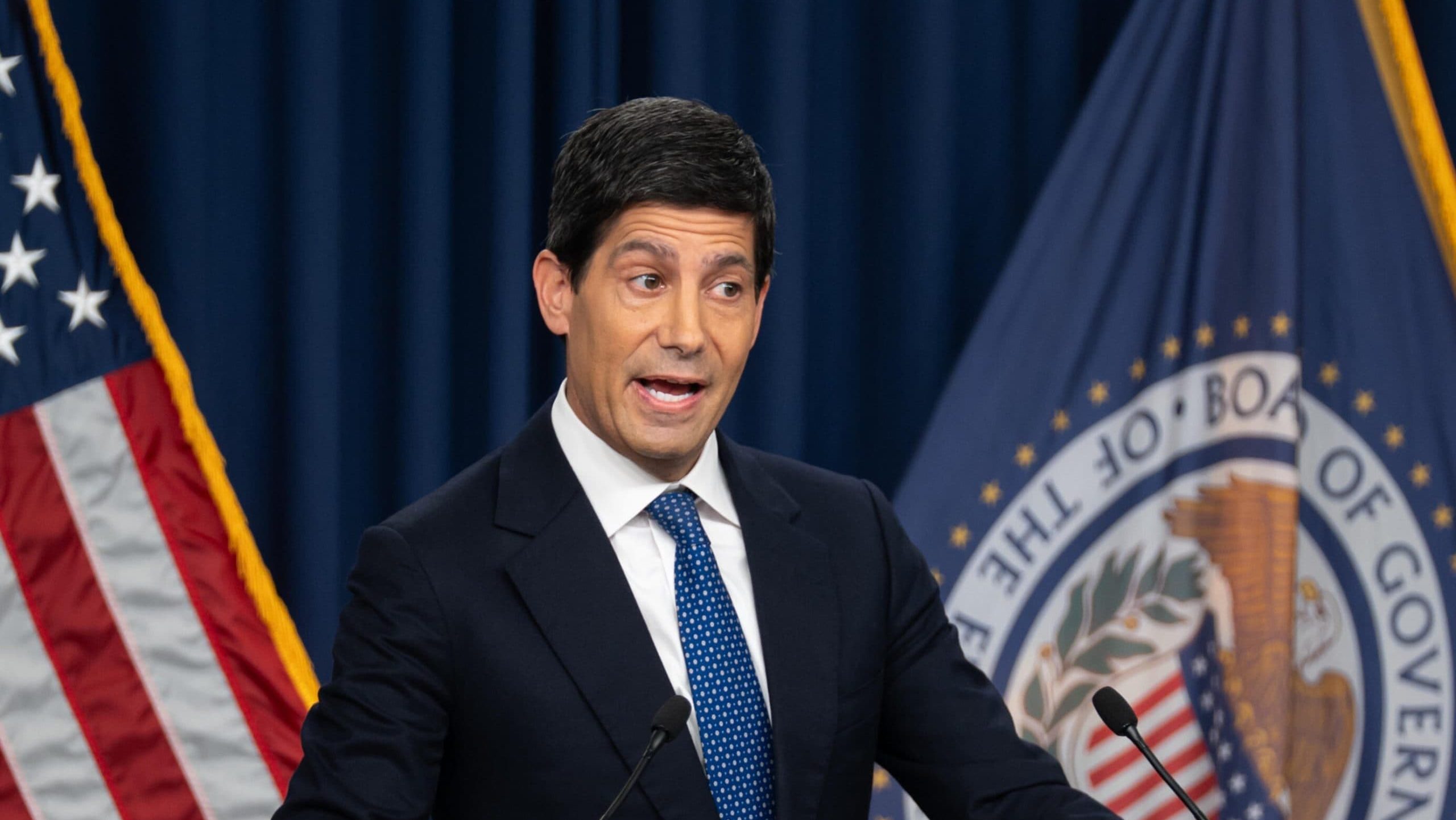 Fed-Chef Kevin Warsh spricht am Rednerpult vor der US-Flagge und der Flagge des Federal Reserve Board
